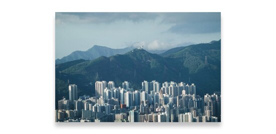 A very modern city at the base of a green hilly back drop.

